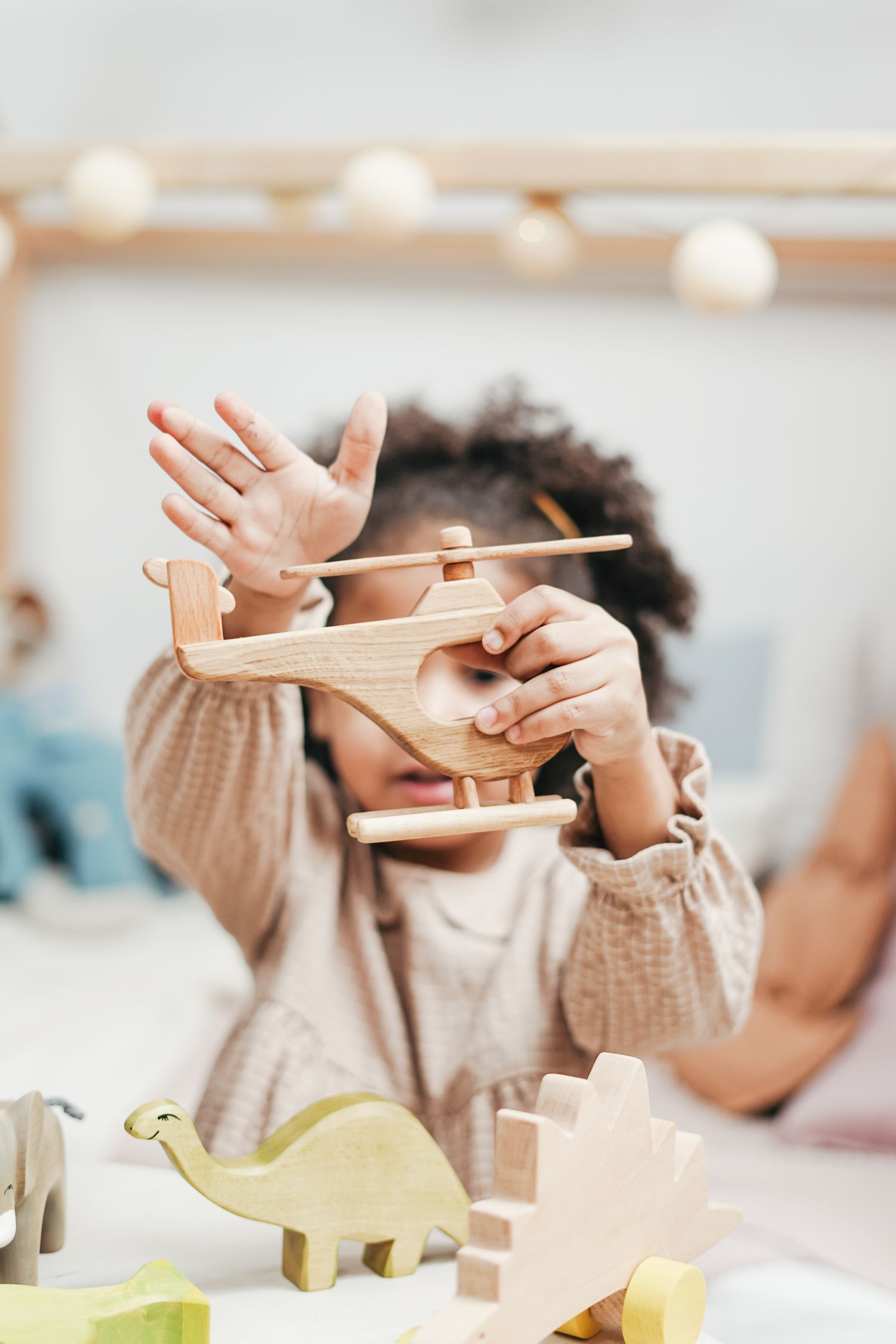 Young child playing with a wooden toy helicopter and wooden animal figures